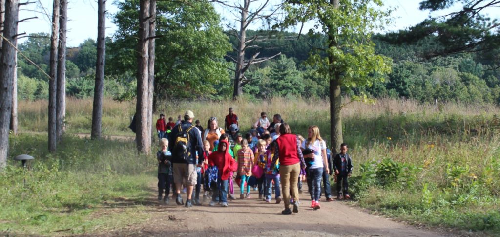 A large group of children and adults walking on a trail at Belwin's Education Center property. 