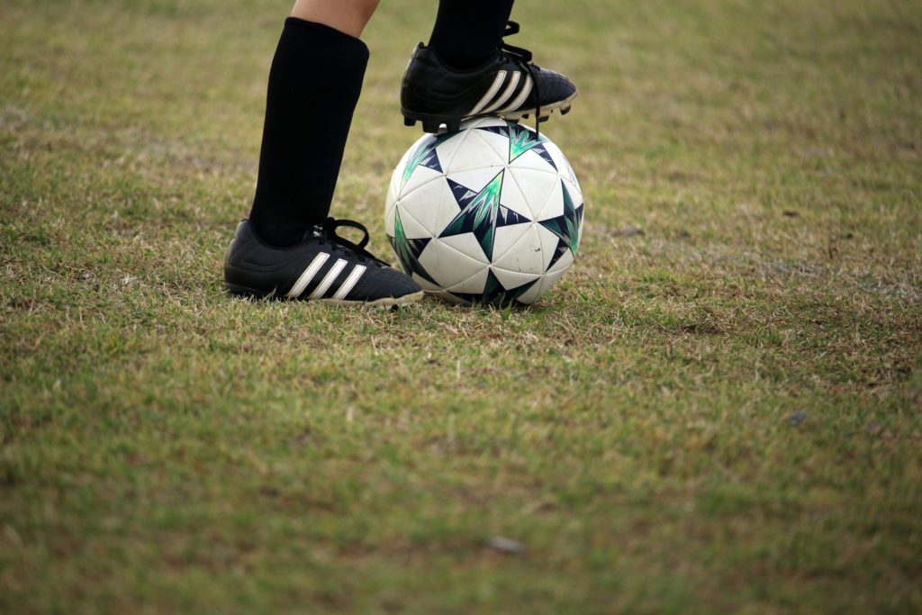 A person wearing soccer cleats with one foot on a soccer ball.