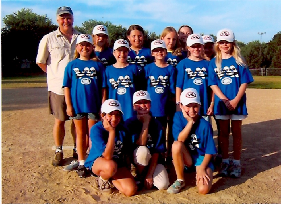 About ten children and one adult wearing matching t-shirts and baseball caps smile towards the camera. 