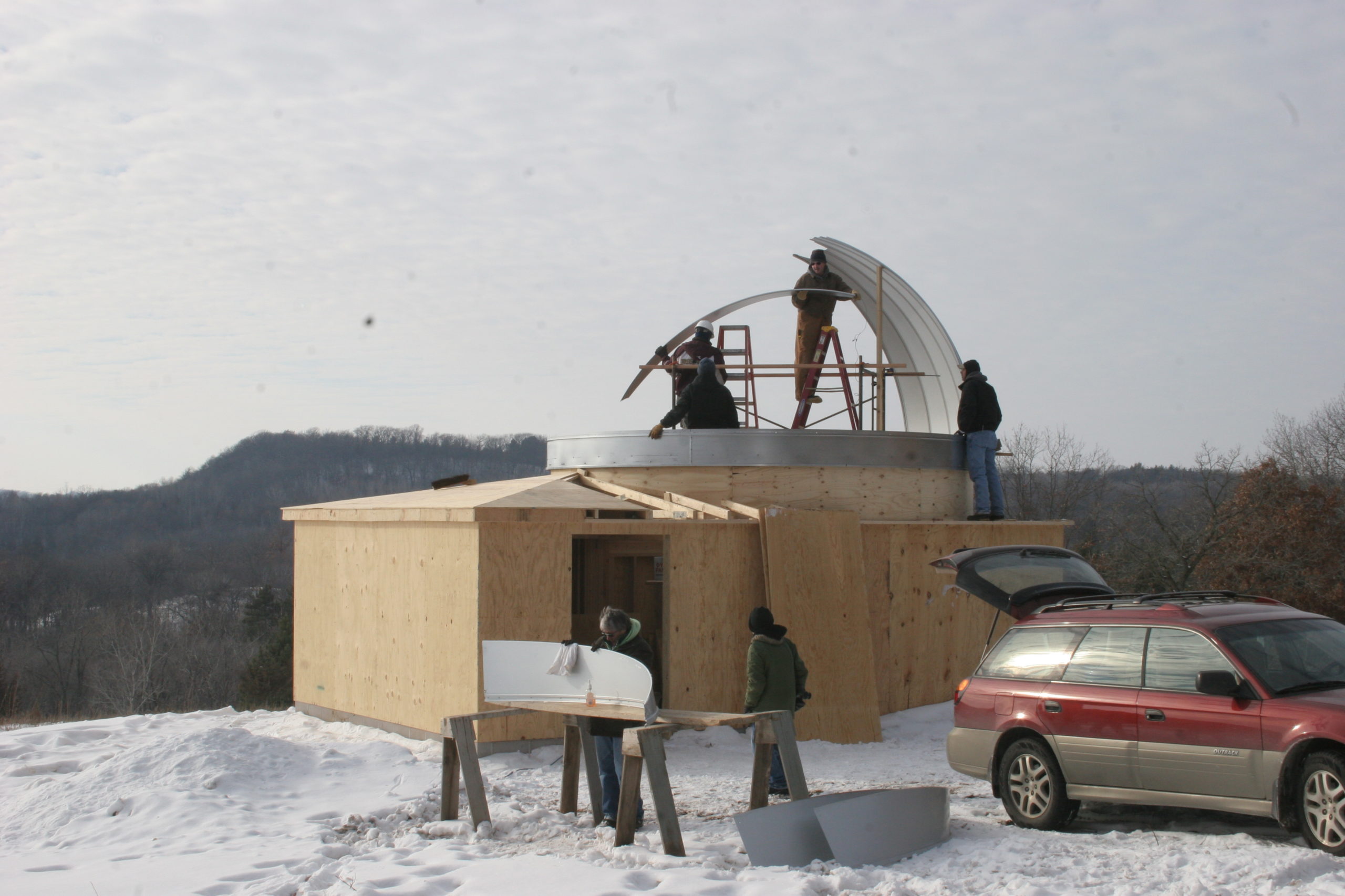Four workers standing on and around a partially built observatory building.