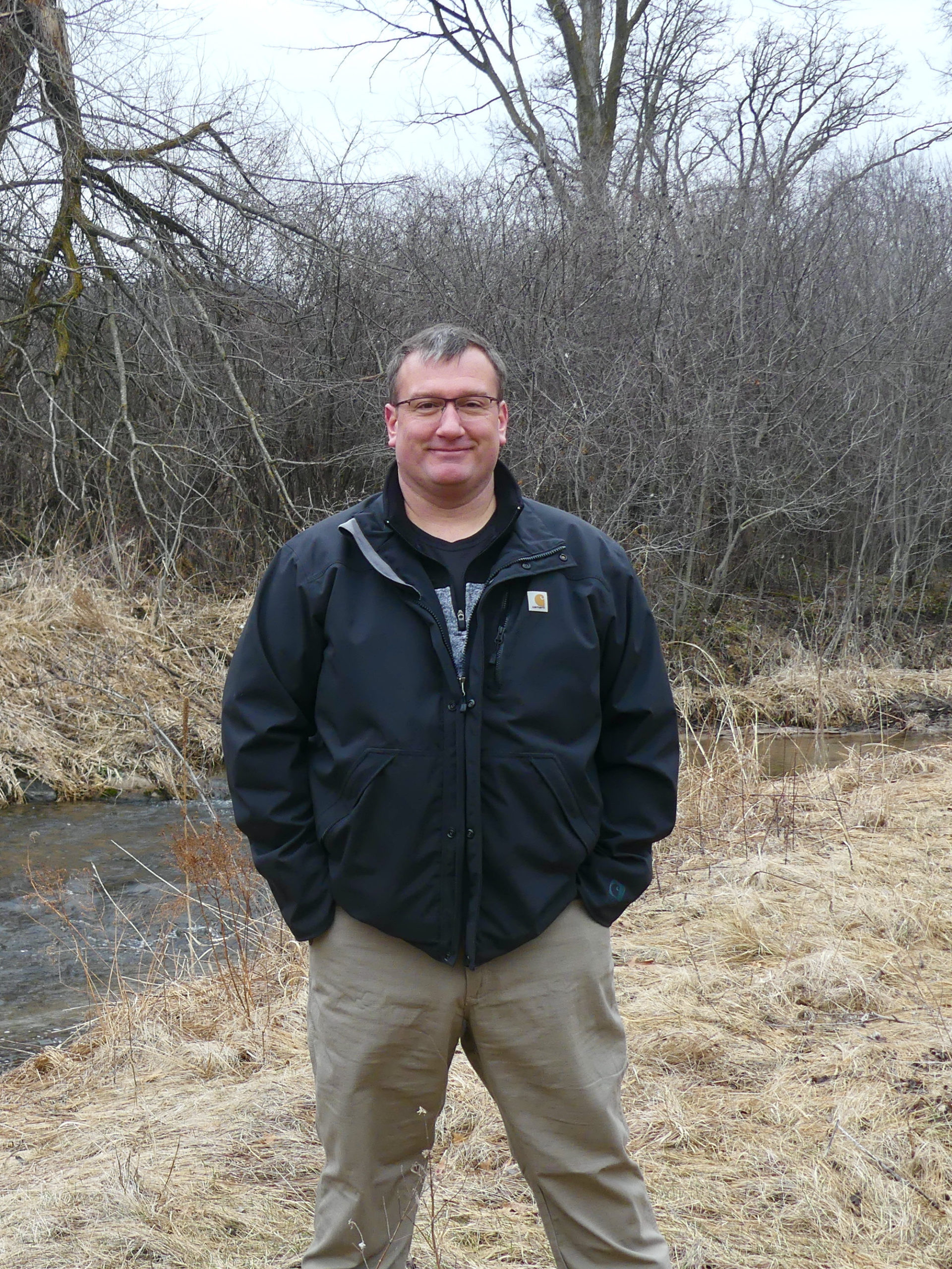 Man wearing jacket, standing in front of creek