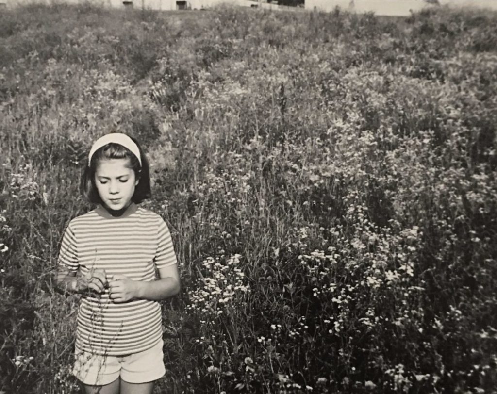 Black and white photo of little girl in front of tall grass